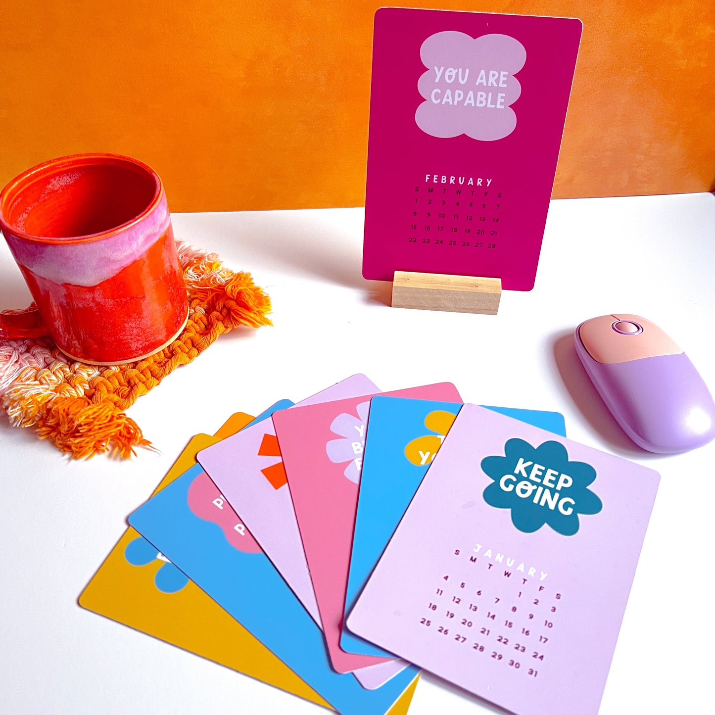 Colorful desk calendar pages with motivational messages on a white surface with an orange background