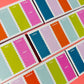 Several small boxes of weekly planner notepads arranged diagonally. They use a scalloped-edge daily labels in pastel and bright colors including blue, green, pink, orange, purple, and light blue, with day names printed on the front.